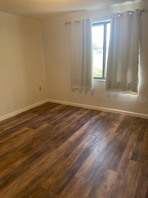 spare room with baseboards and dark wood-style flooring