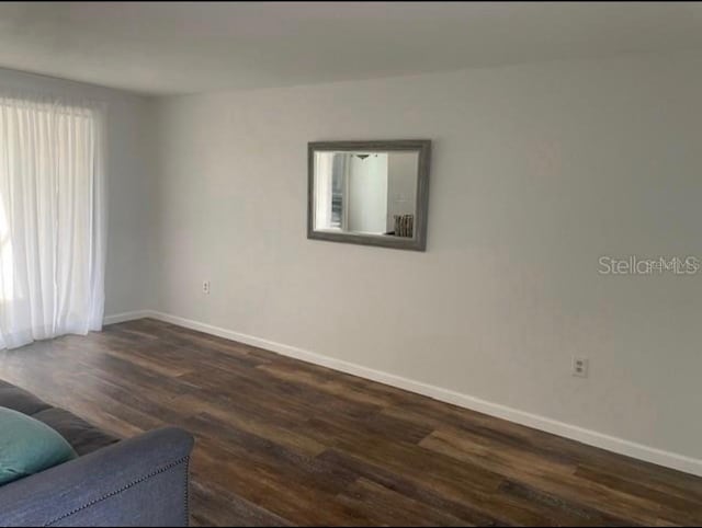 empty room featuring plenty of natural light, dark wood finished floors, and baseboards