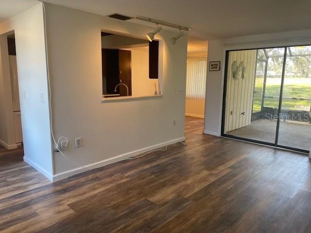 unfurnished room with track lighting, dark wood finished floors, visible vents, and baseboards