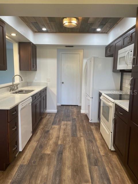 kitchen with white appliances, dark wood-type flooring, light countertops, dark brown cabinets, and a sink