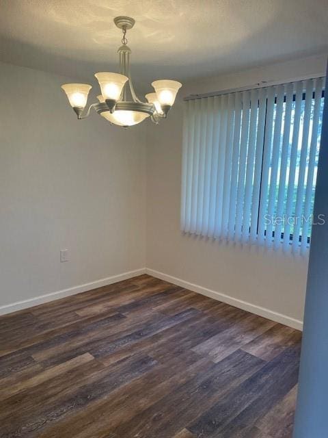 empty room with a chandelier, dark wood-style floors, and baseboards