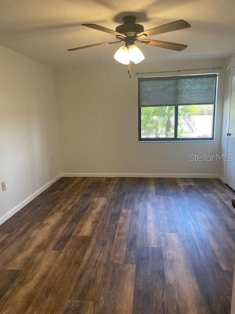 unfurnished room featuring dark wood-style flooring, a ceiling fan, and baseboards