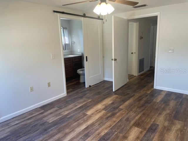 unfurnished bedroom with baseboards, visible vents, dark wood finished floors, and ensuite bathroom