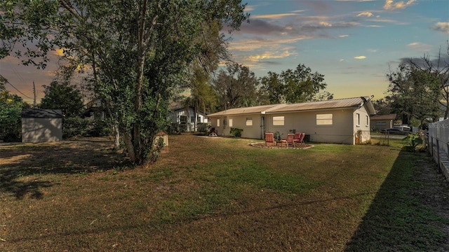 back house at dusk with a lawn, a storage unit, and a fire pit