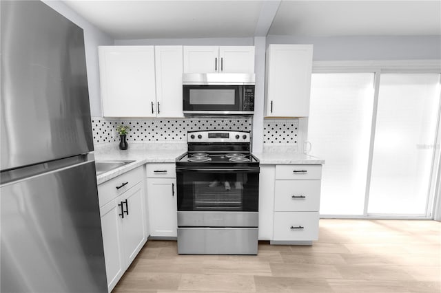 kitchen with backsplash, white cabinets, stainless steel appliances, and light hardwood / wood-style floors