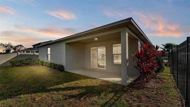 property exterior at dusk featuring a patio area and a lawn