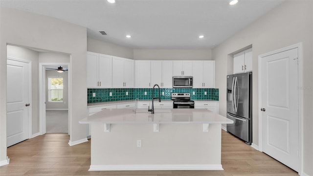 kitchen featuring appliances with stainless steel finishes, an island with sink, backsplash, sink, and white cabinetry