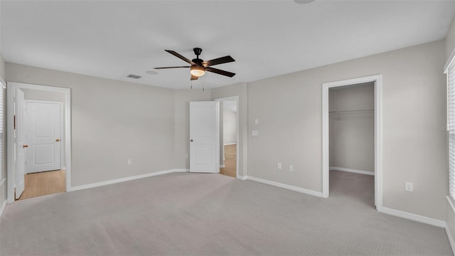 unfurnished bedroom featuring ceiling fan, light carpet, a closet, and a spacious closet