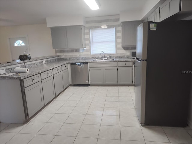 kitchen with gray cabinets, stainless steel appliances, light stone countertops, and sink