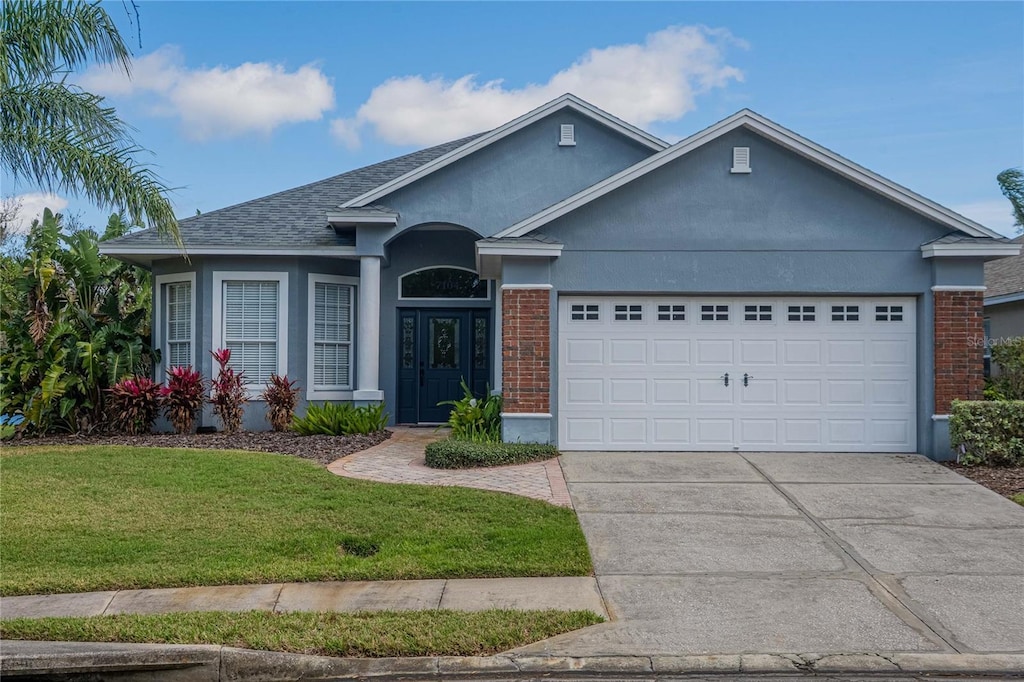 single story home featuring a garage, brick siding, concrete driveway, stucco siding, and a front yard