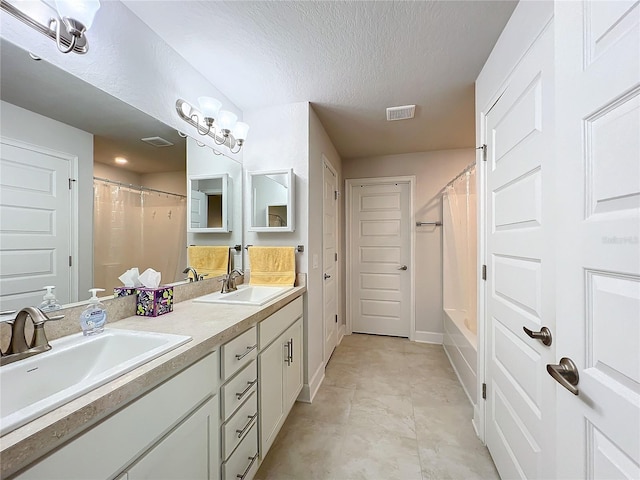 full bathroom with double vanity, a textured ceiling, visible vents, and a sink