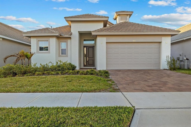 prairie-style home with a garage, decorative driveway, a front yard, and stucco siding