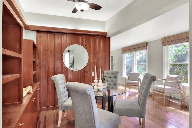 dining space featuring ceiling fan, wood walls, and light wood finished floors