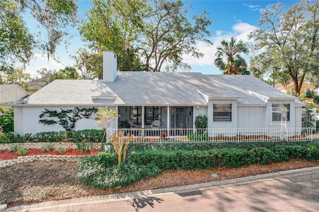 ranch-style house featuring a porch, a chimney, roof with shingles, and fence