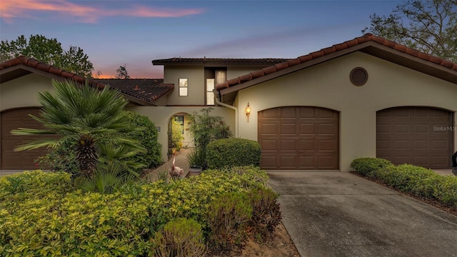 mediterranean / spanish home featuring a garage, driveway, a tiled roof, and stucco siding