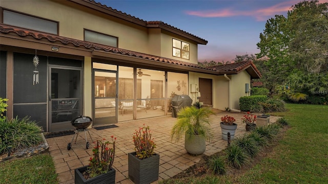 back of property at dusk featuring a patio area, a lawn, and a tiled roof