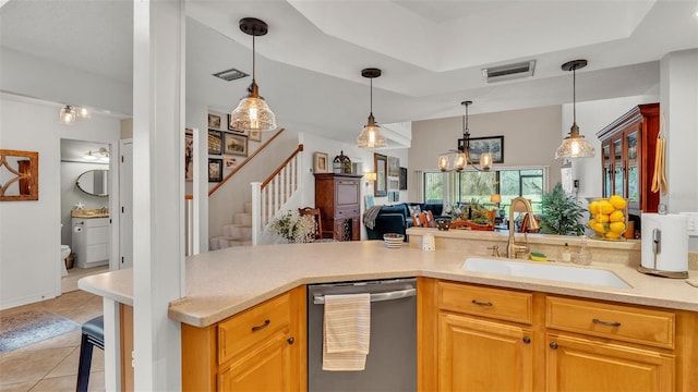 kitchen with a tray ceiling, light tile patterned floors, light countertops, stainless steel dishwasher, and a sink