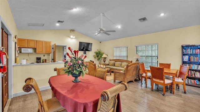 dining room with light wood-style flooring, visible vents, vaulted ceiling, and a ceiling fan