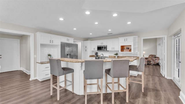 kitchen featuring stainless steel appliances, a breakfast bar, a kitchen island with sink, and white cabinetry