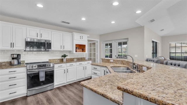 kitchen with white cabinets, light stone counters, appliances with stainless steel finishes, a kitchen island with sink, and a sink