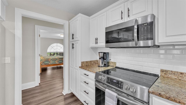 kitchen with light stone counters, stainless steel appliances, dark wood-type flooring, white cabinets, and tasteful backsplash