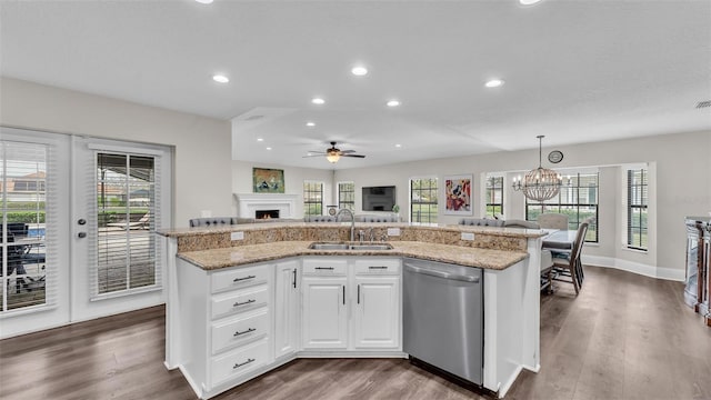 kitchen featuring stainless steel dishwasher, white cabinetry, a sink, an island with sink, and a warm lit fireplace