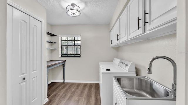 clothes washing area with cabinet space, light wood-style flooring, washing machine and dryer, a sink, and a textured ceiling