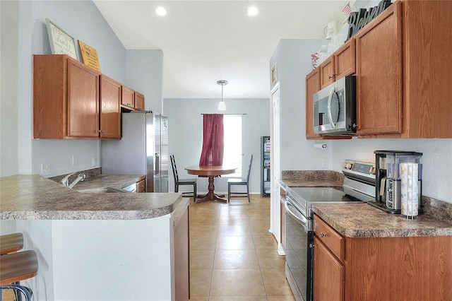 kitchen with a peninsula, a sink, appliances with stainless steel finishes, a kitchen bar, and decorative light fixtures