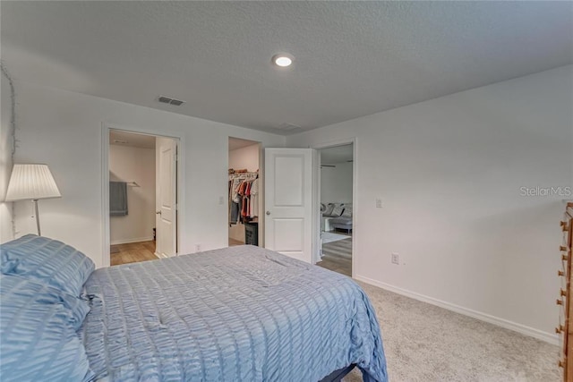 bedroom featuring visible vents, baseboards, light colored carpet, a walk in closet, and a textured ceiling