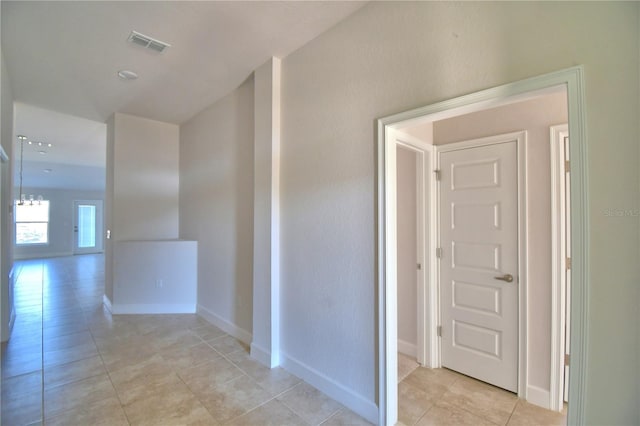 hallway featuring light tile patterned floors, baseboards, and visible vents