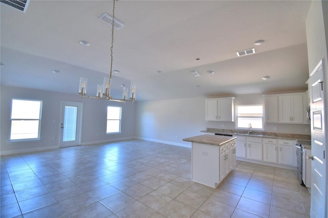 kitchen with open floor plan, a center island, an inviting chandelier, white cabinetry, and a sink