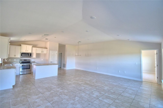 kitchen with lofted ceiling, appliances with stainless steel finishes, white cabinetry, a kitchen island, and a sink