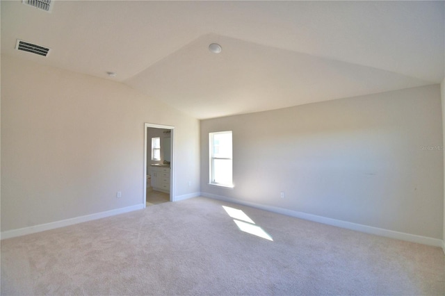 empty room featuring lofted ceiling, visible vents, light carpet, and baseboards