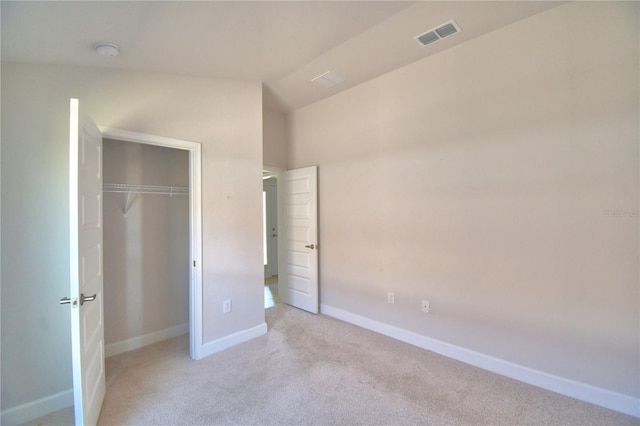 unfurnished bedroom featuring lofted ceiling, a closet, visible vents, light carpet, and baseboards