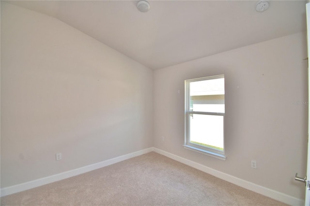 spare room with baseboards, lofted ceiling, and light colored carpet