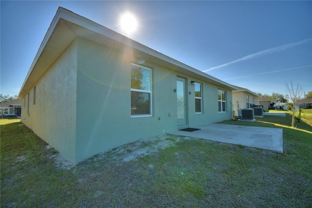 rear view of house featuring a patio, a yard, central air condition unit, and stucco siding