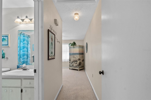 hall featuring a textured ceiling, baseboards, a sink, and light colored carpet