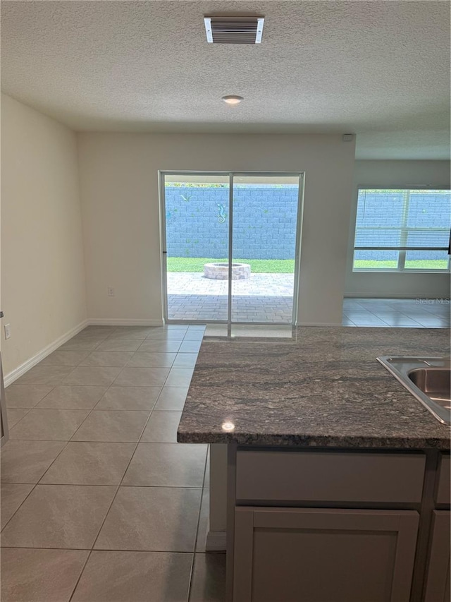6769 SE 3rd Loop, Ocala, FL 34472 - kitchen featuring healthy amount of natural light, a textured ceiling, light tile patterned floors, and dark stone counters