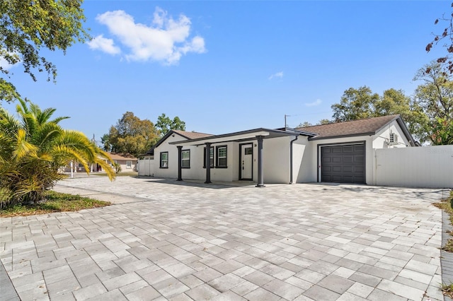 view of front of house featuring stucco siding, decorative driveway, fence, roof with shingles, and a garage