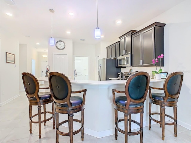 kitchen featuring hanging light fixtures, a breakfast bar, stainless steel appliances, and light countertops