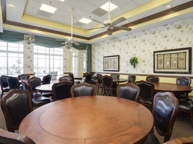 dining room with wallpapered walls, crown molding, a tray ceiling, and a ceiling fan