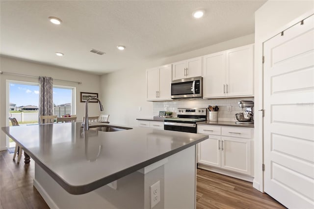 kitchen with visible vents, dark countertops, stainless steel appliances, white cabinetry, and a sink