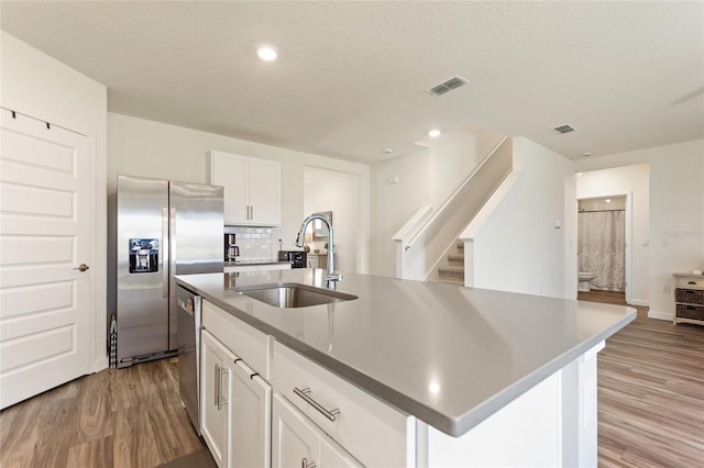 kitchen featuring white cabinets, light wood-style flooring, appliances with stainless steel finishes, a kitchen island with sink, and a sink