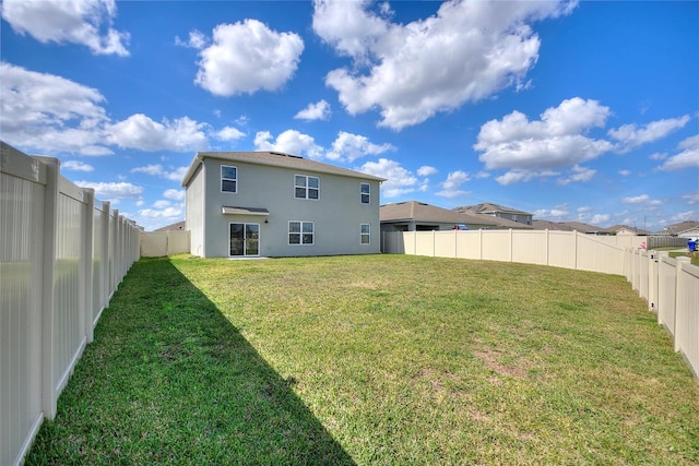 back of house with stucco siding, a fenced backyard, and a yard