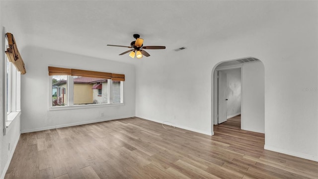 empty room with arched walkways, ceiling fan, wood finished floors, and visible vents