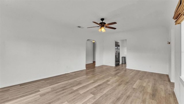 unfurnished room with light wood-type flooring, arched walkways, visible vents, and a ceiling fan