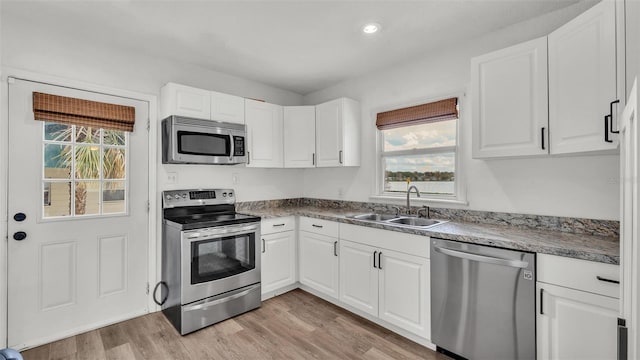 kitchen with light wood-style flooring, appliances with stainless steel finishes, white cabinets, and a sink