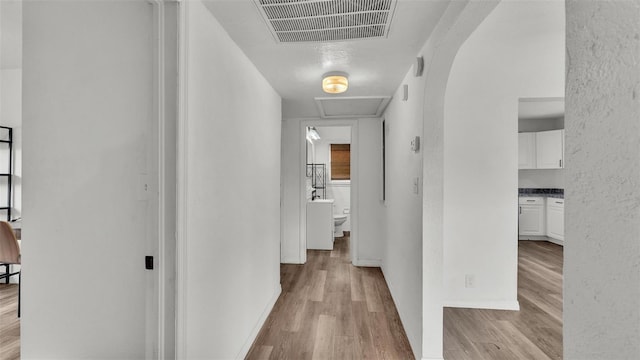 hall with light wood-style floors, baseboards, visible vents, and a textured wall