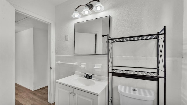 bathroom with tile walls, a textured wall, toilet, vanity, and wood finished floors