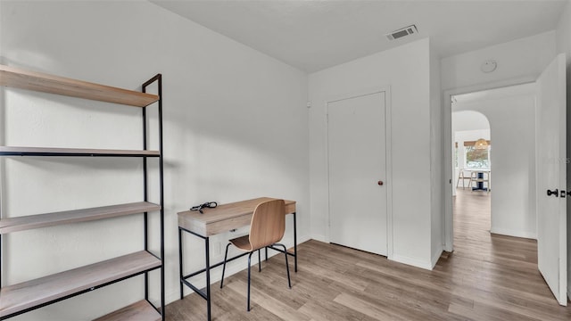 office with baseboards, visible vents, arched walkways, and wood finished floors